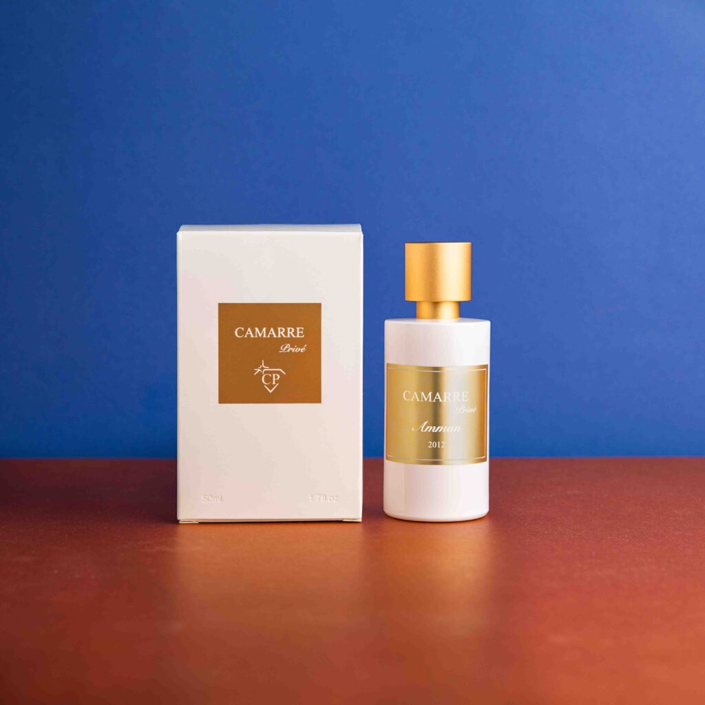 photo de produit, packshot d'un parfum avec sa boîte au centre de l'image. boîte blanche avec un carré doré au centre avec le logo et le nom de la marque. Flacon de parfum à droite de la boîte blanc avec une etiquette et un bouchon doré. Photographe