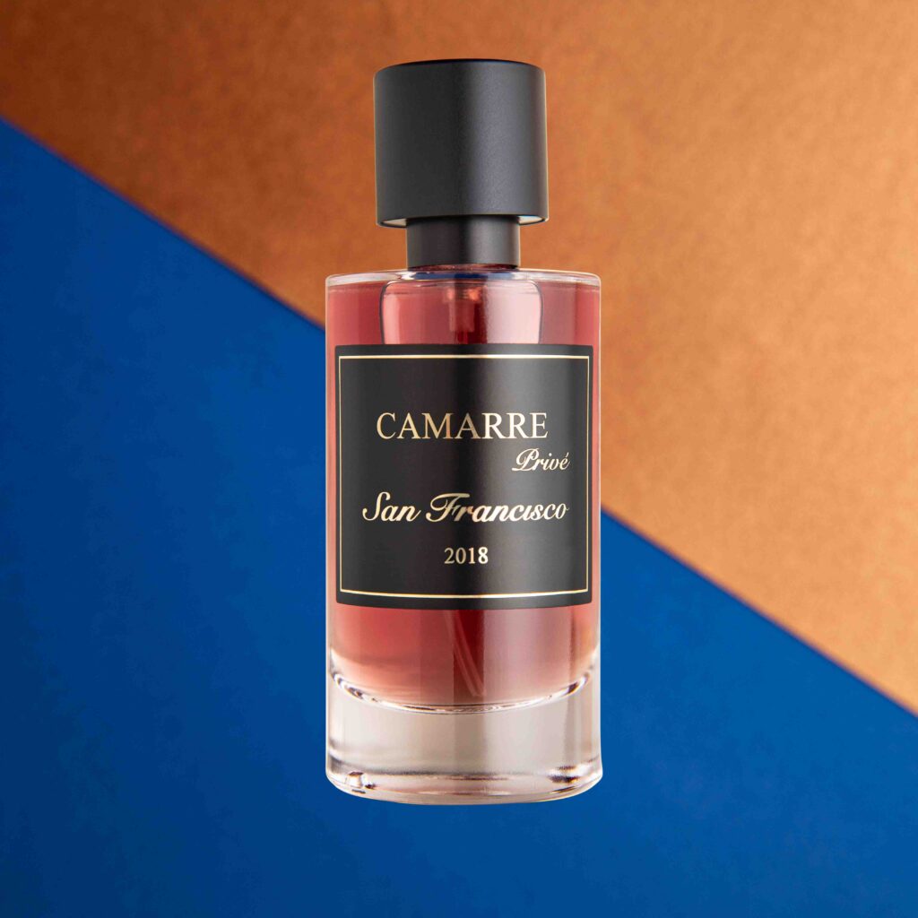 photo de produit, photo de parfum de la gamme cammare, flacon de parfum transparent avec une eau de parfum rose. Bouchon noir. Arrière plan avec deux couleur qui coupent l'image en diagonale avec des tons cuivre et bleu roi. Photographe